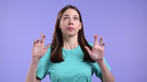 Roztomilá žena modlí se zkříženými prsty přes fialové pozadí. Dívka prosit někoho uspokojit své touhy, pomoci s. — Stock video