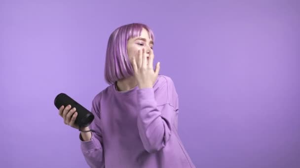 Unusual woman with dyed violet hairstyle listening to music by wireless portable speaker - modern sound system. Young girl dancing, enjoying on purple studio background — Stock Video