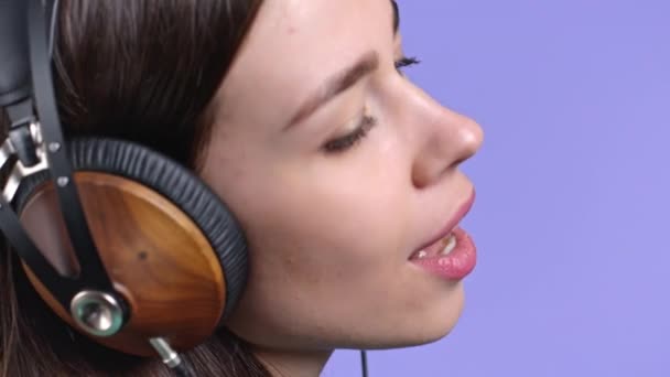 Mooie vrouw die naar muziek luistert, zingt met een koptelefoon op een violette studio achtergrond. Schattig meisjes portret. Radio, geluk, vrijheid, jeugdconcept. — Stockvideo
