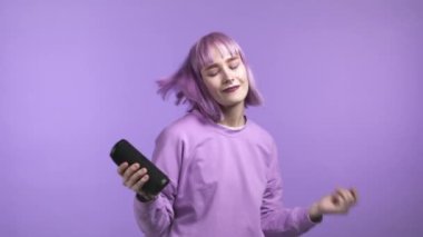 Kablosuz taşınabilir hoparlörden müzik dinleyen, menekşe rengi saç stiline sahip alışılmadık bir kadın. Modern ses sistemi. Genç kız dans ediyor, mor stüdyoda eğleniyor.