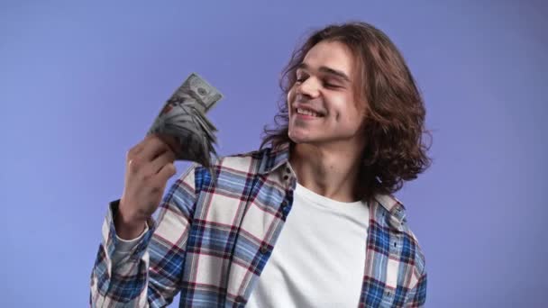 Zadowolony człowiek z dolarami. Szczęśliwy podekscytowany facet pokazujący pieniądze - banknoty dolarowe na fioletowej ścianie. Symbol sukcesu, zysku, zwycięstwa. — Wideo stockowe