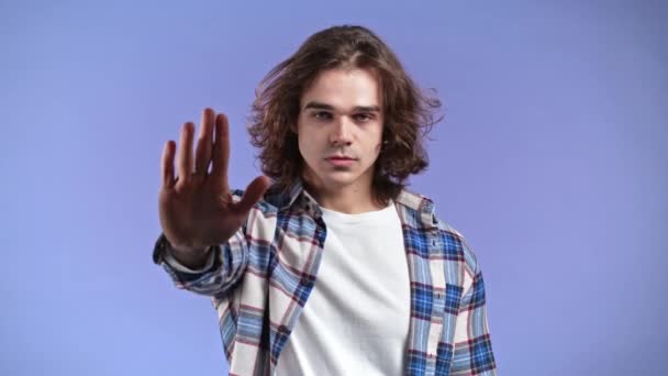 Retrato de homem sério mostrando gesto de rejeição por sinal de mão stop palm. Cara com penteado longo isolado no fundo violeta. — Vídeo de Stock