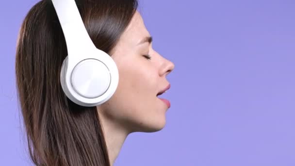 Aantrekkelijke vrouw met witte koptelefoon op violette studio achtergrond. Schattig meisjes portret. Muziek, radio, geluk, vrijheid, jeugdconcept. — Stockvideo