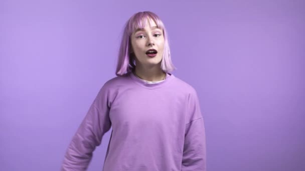 Vänlig kvinna viftar med handen - hej. Hälsning, säg hej till kameran. Vacker ung flicka med färgat lila hår på violett studio bakgrund. — Stockvideo