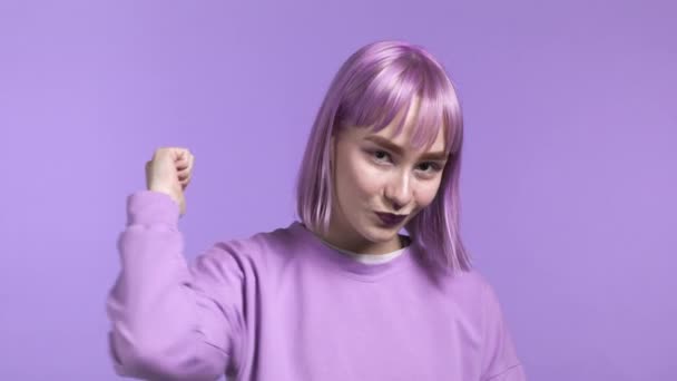 Vacker kvinna visar tummen upp som skylt över violett studio bakgrund. Positiv ung flicka med färgat lila hår ler mot kameran. Vinnare. Framgång. Kroppsspråk. — Stockvideo