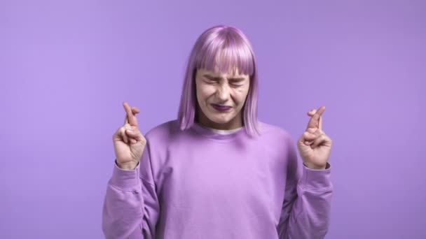 Donna piuttosto alla moda che prega su sfondo viola. Ragazza con i capelli viola tinti implorando Dio con le dita incrociate per realizzare i suoi sogni, aiutare con. — Video Stock