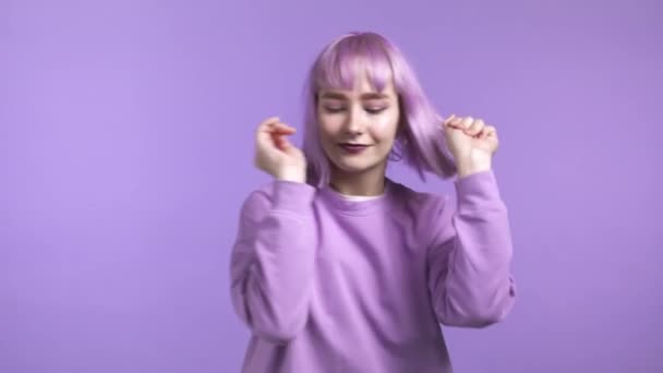 Atrakcyjna kobieta z fioletową fryzurą tańcząca na fioletowym tle studia. Dziewczyna zoomer w pozytywnym nastroju. — Wideo stockowe