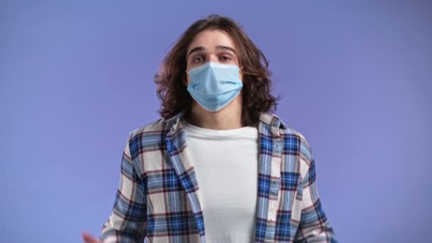 Onverschillige onzekere man met een beschermend gezichtsmasker maakt gebaar van ik weet het niet, kan niets helpen. Moeilijk vraagconcept. Violette studio achtergrond — Stockvideo