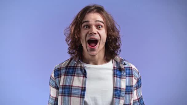 Man depicts amazement, shows WOW delight face effect. Surprised excited happy guy with curly long hairdo. Handsome male shocked model on violet background. — Stock Video