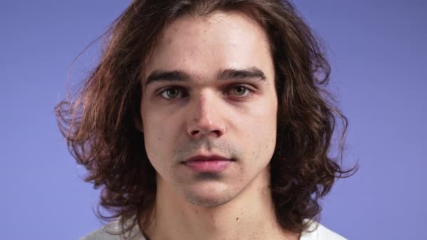 Portrait of serious european man looking to camera. Young handsome guy with long hairdo on violet studio background. — Stock Video