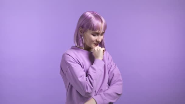 Young shy woman with dyed violet hairstyle looking to camera, flirting. Beautiful model girl on purple studio background. — Stock Video