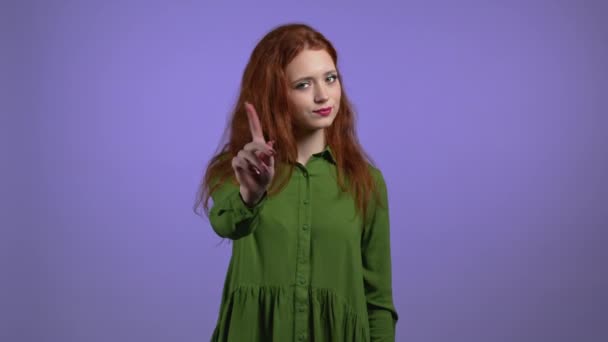 Portrait of serious woman showing rejecting gesture by stop finger sign. Girl with red curly hair isolated on violet background. — Stock Video