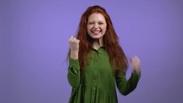 Mulher com cabelo vermelho é muito feliz e feliz, ela mostra sim gesto de vitória, ela alcançou o resultado, objetivos. Surpreendido feliz senhora animado em fundo estúdio violeta. Conceito de jackpot. — Vídeo de Stock