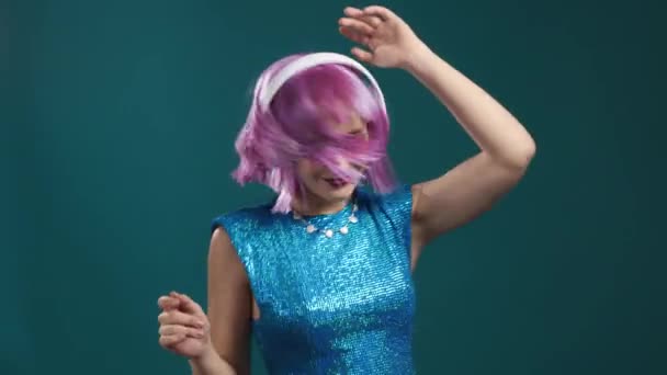 Atraktivní moderní žena tančí se sluchátky na modrém pozadí studia. Roztomilý fialový portrét obarvených holek. Hudba, rádio, párty koncept. — Stock video