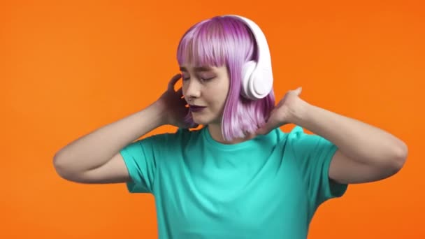 Millenial vrouw met geverfd violet kapsel dansen met koptelefoon op oranje studio achtergrond. Schattig meisjes portret. Muziek, radio, geluk, vrijheid, jeugdconcept. — Stockvideo