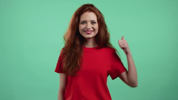 Vacker kvinna visar tummen upp som skylt över grön studio bakgrund. Positiv ung flicka med naturligt hår ler mot kameran. Vinnare. Framgång. Kroppsspråk. — Stockvideo