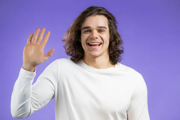 Jeune homme amical agitant la main - bonjour. Salut, dis bonjour à la caméra. Guy sur fond de studio violet. — Photo