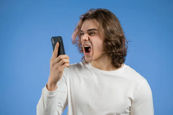 Злой человек в белой футболке, кричащий по мобильному телефону. Стресс и депрессивный парень на синем фоне. — стоковое фото