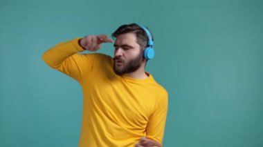 Sakallı yakışıklı, kablosuz kulaklıklı müzik dinleyen, stüdyoda eğlenen, mavi arka planda dans eden bir adam. Dans, radyo konsepti.