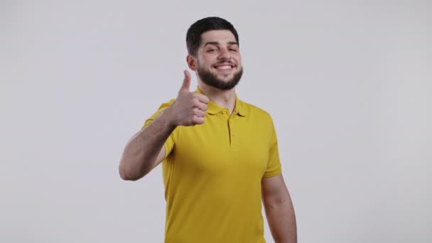 Um homem bonito de amarelo mostra o polegar para cima, como um gesto. Um tipo feliz com um fundo branco. Vencedor. Sucesso. Modelo masculino positivo sorri para a câmera. Linguagem corporal. — Vídeo de Stock