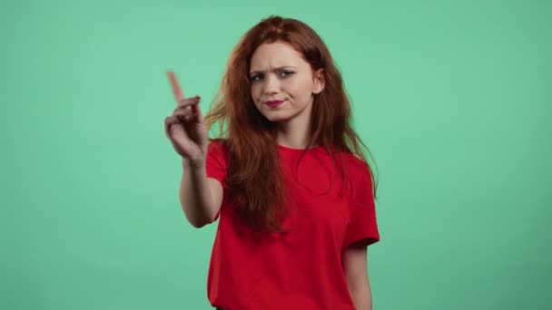 Egy komoly nő portréja, amint elutasító gesztust mutat a mutatóujjával. Lány elszigetelt zöld háttér. — Stock videók