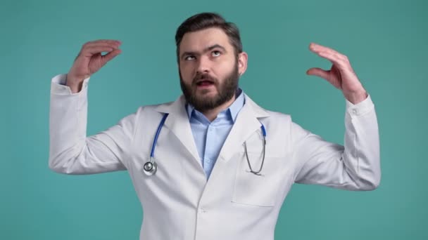 Handsome bored doctor man in medical coat showing bla-bla-bla gesture with hands and rolling eyes isolated on blue background. Empty promises, blah concept. Lier. — Stock Video