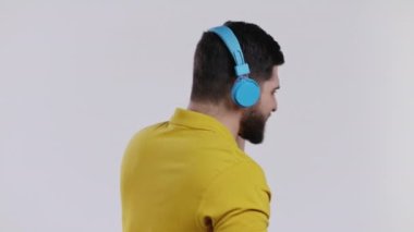 Kablosuz kulaklıkla müzik dinleyen, eğlenen, stüdyoda beyaz arka planda dans eden aktif bir genç. Dans, radyo konsepti.