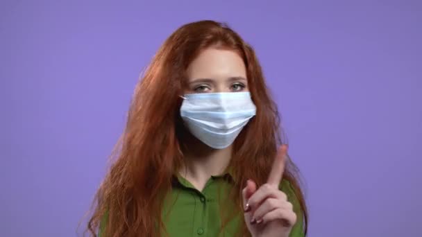 Retrato de una mujer seria con máscara protectora que muestra gesto de rechazo por señal de stop finger. Chica aislada sobre fondo violeta. — Vídeos de Stock