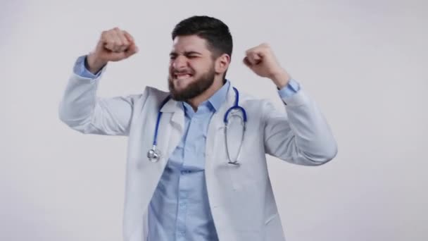 Szczęśliwy doktor zabawny taniec, sukces i szczęście w pracy. Przystojny lekarz z brodą w profesjonalnym medycznym białym płaszczu pokazuje tak gest izolowany na białym tle studia. — Wideo stockowe