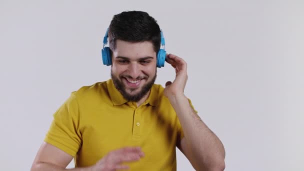 Active young man listening to music with wireless headphones, guy having fun, dancing in studio on white background. Dance, radio concept. — Stock Video