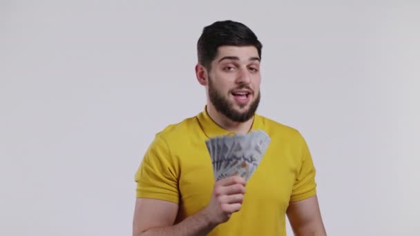 Ευτυχισμένος ενθουσιασμένος άνθρωπος με μετρητά χρήματα - δολάρια ΗΠΑ χαρτονομίσματα σε λευκό τοίχο. Σύμβολο του τζάκποτ, κέρδος, νίκη, κερδίζοντας το λαχείο — Αρχείο Βίντεο
