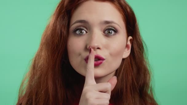 Leende kvinna håller fingret på sina läppar över grön bakgrund. Gest av shhh, hemlighet, tystnad. Närbild — Stockvideo
