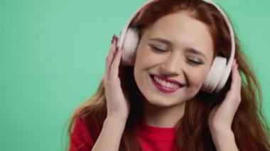 Yeşil stüdyo arka planında beyaz kablosuz kulaklıklı çekici bir kadın. Şirin kızlar portresi. Müzik, radyo, mutluluk, özgürlük, gençlik kavramı.