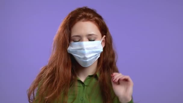 Hermosa mujer en máscara protectora médica bailando enérgica y activamente sobre fondo de estudio violeta. Fiesta, felicidad, libertad, concepto de juventud. — Vídeos de Stock