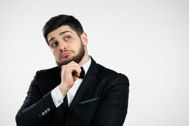 Düşünen adam beyaz arka plana bakıyor. Düşünceli yüz ifadeleri. Siyah smokinli yakışıklı sakallı adam.