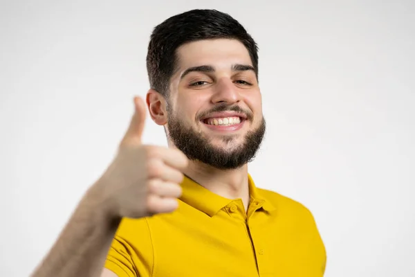 Schöner Mann in gelbem Gewand zeigt Daumen hoch wie Geste. Glücklicher Kerl auf weißem Hintergrund. Sieger. Mit Erfolg. Positives männliches Model lächelt in die Kamera. Körpersprache. — Stockfoto