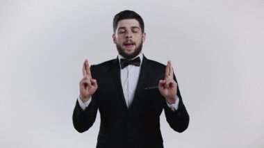 Beyaz arka planda dua eden genç beyaz bir adam. Siyah smokinli adam, birine arzularını tatmin etmesi için yalvarıyor..