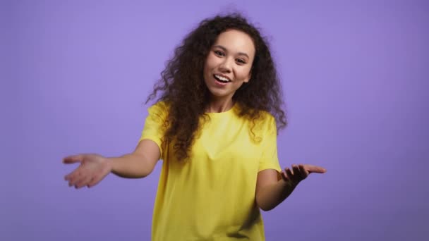 Young woman showing - Hey you, come here. Pretty girl in yellow wear ask join her,beckons with inviting hand hugs gesture.She is looking playful flirtatious, inviting to come.Violet studio background. — Stock Video