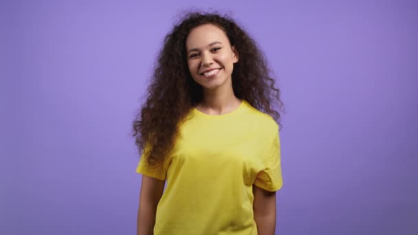 Jeune femme aux cheveux bouclés regardant vers la caméra, souriant. Belle dame modèle mixte de race sur fond de studio violet. Portrait adolescent. — Video