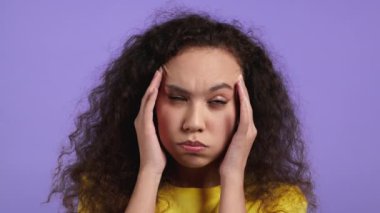 Başı ağrıyan kadın portresi, Violet stüdyo portresi. Kız ellerini başının üstüne koyuyor, şakaklara masaj yapıyor. Migren sorunları, ilaç, hastalık kavramı