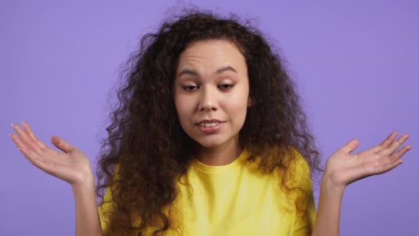 Indifferent unsure woman makes gesture of I dont know, cant help anything. Difficult question concept. Girl with curly hair on violet studio background. — Stock Video