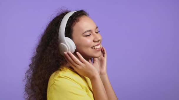 Sluiten aantrekkelijke vrouw met witte draadloze hoofdtelefoon op violette studio achtergrond. Schattig meisje dat zingt en danst met haar hoofd. Muziek, radio, geluksconcept. — Stockvideo