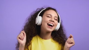 Violet stüdyosunun arka planında beyaz kablosuz kulaklıklı tatlı genç kız. Genç bayan portresi. Müzik, radyo, mutluluk, özgürlük, gençlik kavramı.