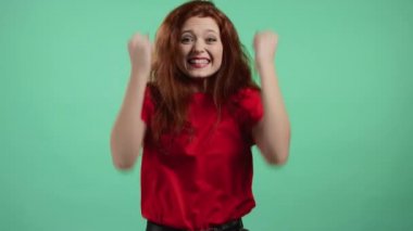 Kızıl saçlı kadın çok mutlu ve mutlu. Zaferin evet jestini gösteriyor. Sonuç elde etti. Yeşil stüdyo geçmişindeki şanslı bayana şaşırdım. Büyük ikramiye konsepti.