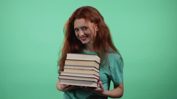 Studentka drží hromadu univerzitních knih z knihovny na zeleném pozadí ve studiu. Žena se usmívá, je šťastná, že odmaturovala. — Stock video