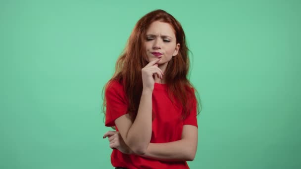 Denkende vrouw die opkijkt naar groene studio achtergrond. Pensieve gezichtsuitdrukkingen. Mooi model met aantrekkelijk uiterlijk en rood natuurlijk haar. — Stockvideo