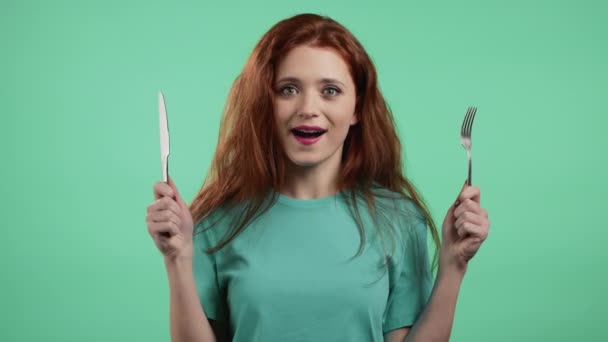 Portrait of hungry woman with fork and knife. Lady waiting for serving dinner dishes with cutlery on green studio background. — Stock Video