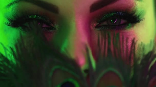 Female face with peacock feathers. Woman with beautiful make-up, glitter sparkling eyeshadows. Girl blinking with green eyes and false lashes. Beauty, cosmetics, art, feminine concept. — Stock Video