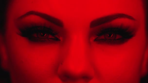 Cara femenina solo bajo la luz roja colorida. Mujer con hermoso maquillaje, brillantes sombras de ojos brillantes. Chica parpadeando con ojos verdes, contrayéndose. Belleza, cosmética, arte, concepto femenino. — Vídeo de stock