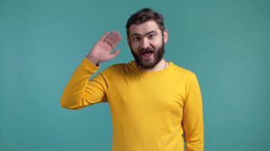 Genç adam el sallıyor. Merhaba. Selamlar, kameraya merhaba deyin. Mavi stüdyo geçmişinde sakalı olan adam..